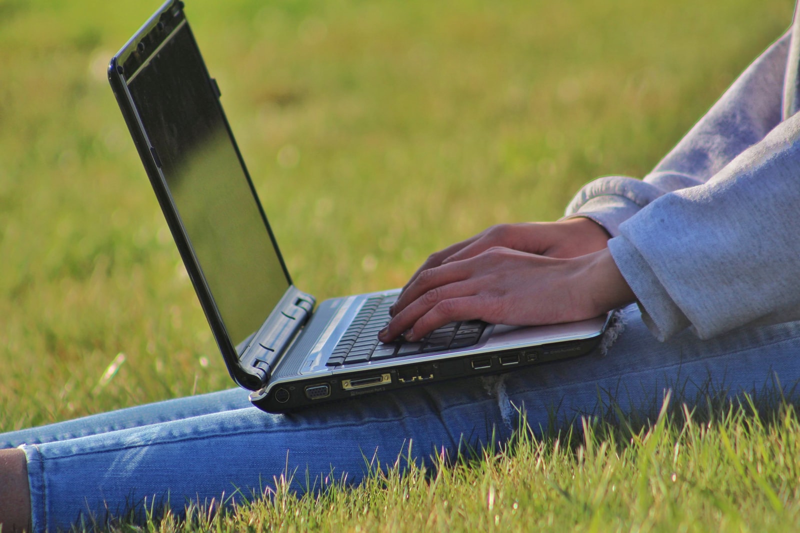 person in blue denim jeans using black laptop computer on green grass field during daytime